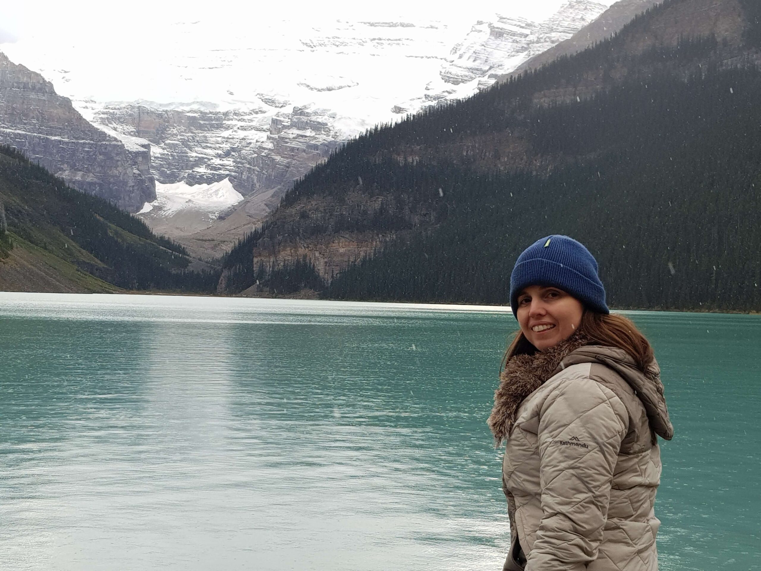 Travel Writer, Crystal Lobban wearing a beanie and coat at Lake Louise in Canada with snowflakes falling.