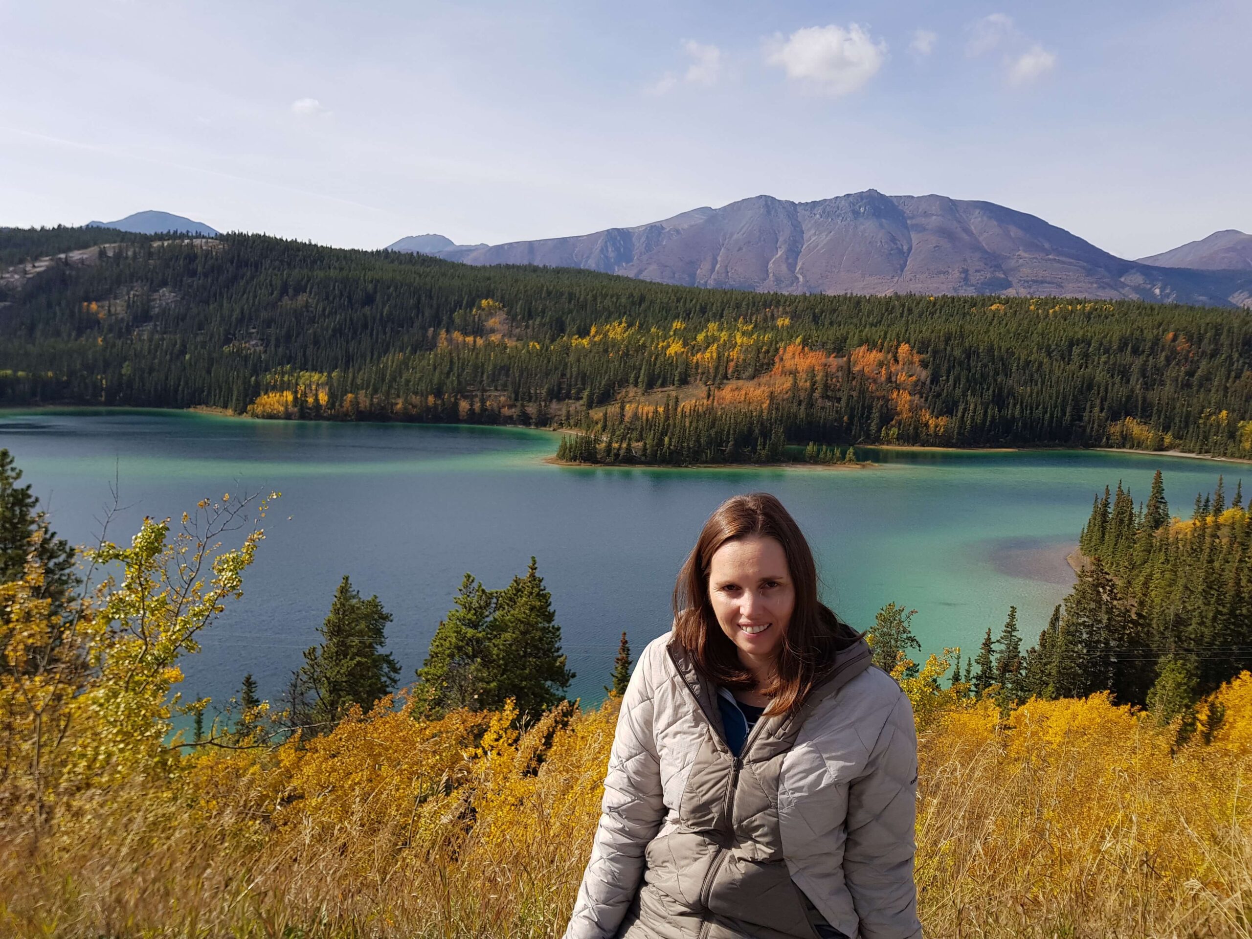 Travel Writer, Crystal Lobban, sitting in the Yukons in Canada with an emerald green lake in the background.