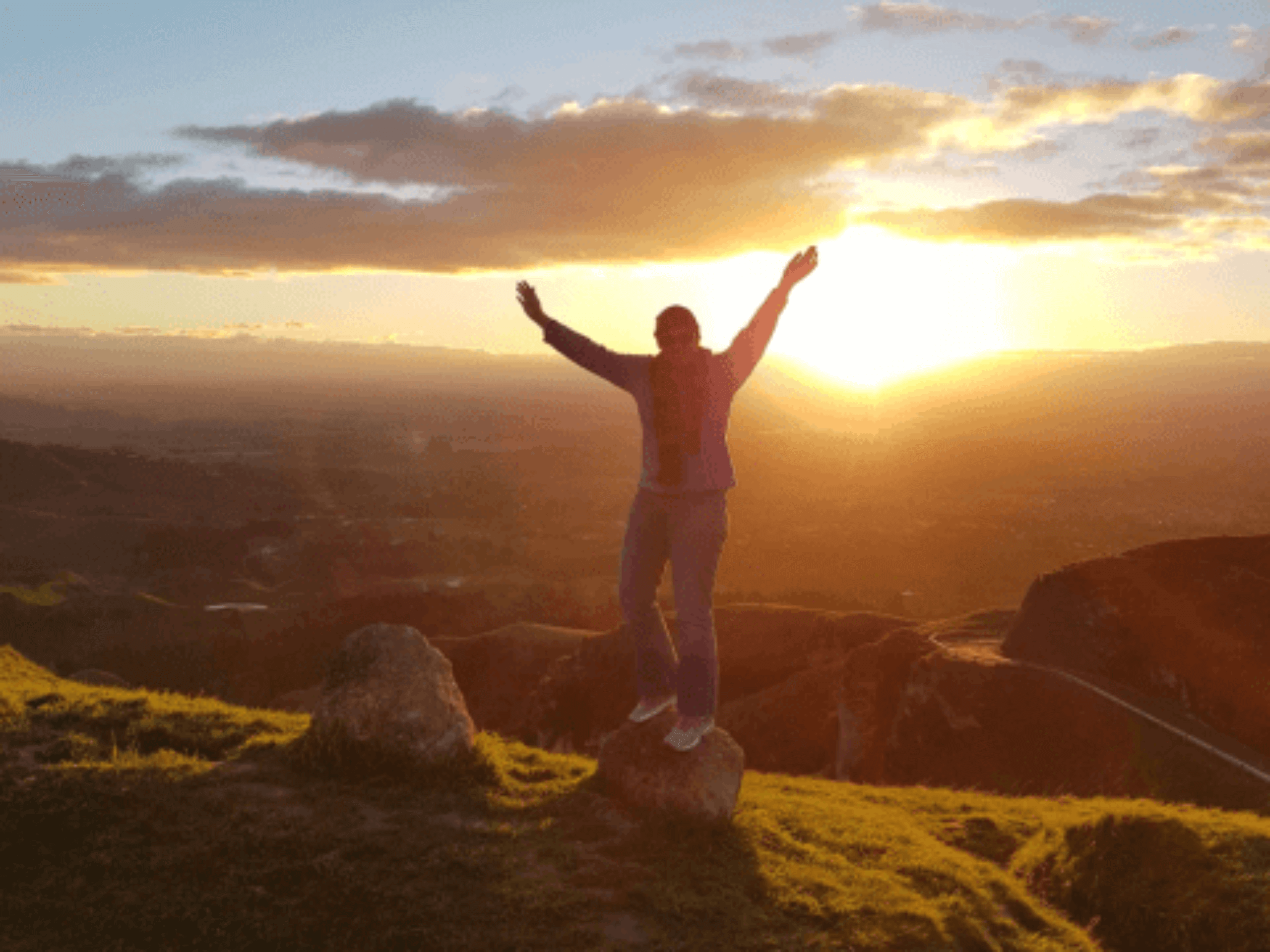 Travel Writer, Crystal Lobban, standing on a rock at Te Mata Peak in New Zealand with the sun setting behind.